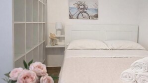 A neatly arranged bedroom with a bed, a nightstand, a lamp, a vase with flowers, and a painting on the wall. - Maty's House 2 steps from the sea (40 mt) (Reggio Calabria)