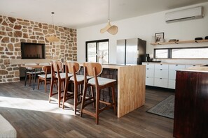 A modern kitchen with a stone wall, wooden dining chairs, a large island, and built-in appliances. - Sparrow House and Carolina Cottage- 2 lakeview homes, Sleeps 18 (Garfield)