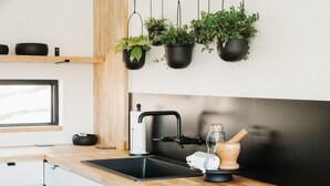 A kitchen with a black sink, wooden countertop, hanging black pots with plants, and a wooden cutting board with a knife. - Sparrow House and Carolina Cottage- 2 lakeview homes, Sleeps 18 (Garfield)