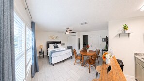 Quarto de hotel com cama, mesa de jantar com cadeiras, ventilador de teto e vista para o exterior.