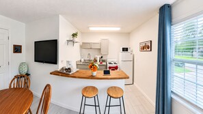 A compact kitchen with a central island, a dining area with wooden furniture, and a large window with blinds. - Private Studio | Near Baptist & Mayo | Fast WiFi (Jacksonville)