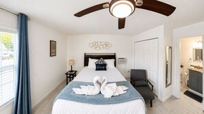 A hotel room with a bed, a ceiling fan, a bedside table with a lamp, a chair, and a bathroom visible through an open door. - Private Studio | Near Baptist & Mayo | Fast WiFi (Jacksonville)