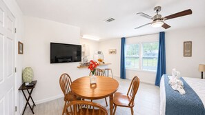 A hotel room with a dining area, a bed with a blue blanket, a TV mounted on the wall, and a ceiling fan. - Private Studio | Near Baptist & Mayo | Fast WiFi (Jacksonville)