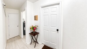 A hallway with a white door, a small table with a vase of flowers, and a sign with the word 'BE' on the wall. - Private Studio | Near Baptist & Mayo | Fast WiFi (Jacksonville)