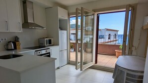 Een moderne keuken met een magnetron, fornuis en kasten, die uitkomt op een balkon met uitzicht op zee.
