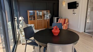 Een moderne woonkamer met een ronde tafel, stoelen, een bank, een houten kast, een ventilator en een televisie.