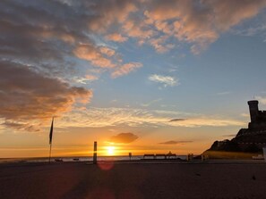 A beach with a sunset, a lifeguard tower, and a distant rocky outcrop. - EVH103 Complete apartment with terrace and parking (Tossa de Mar)