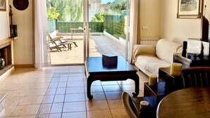 A living room with a sofa, a coffee table, and a dining table. There is a sliding glass door leading to a patio with outdoor furniture. - EVH114 Terraced House with Communal Areas (Altafulla)