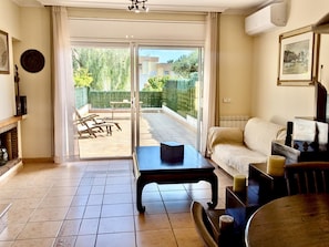 A living room with a sofa, a coffee table, and a dining table. There is a sliding glass door leading to a patio with outdoor furniture.