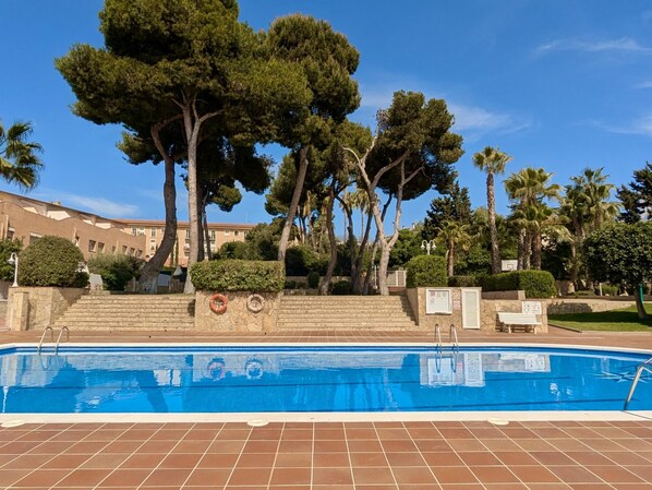 A swimming pool with steps leading up to it, surrounded by trees and a building in the background.