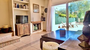 A living room with a TV, shelves with books and decorative items, a fireplace, and a view of the outdoors. - EVH114 Terraced House with Communal Areas (Altafulla)