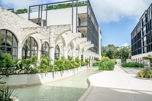 A modern building with stone arches, a water feature, and greenery. - Moonlight Suite · Balcony · Tulum (Tulum)