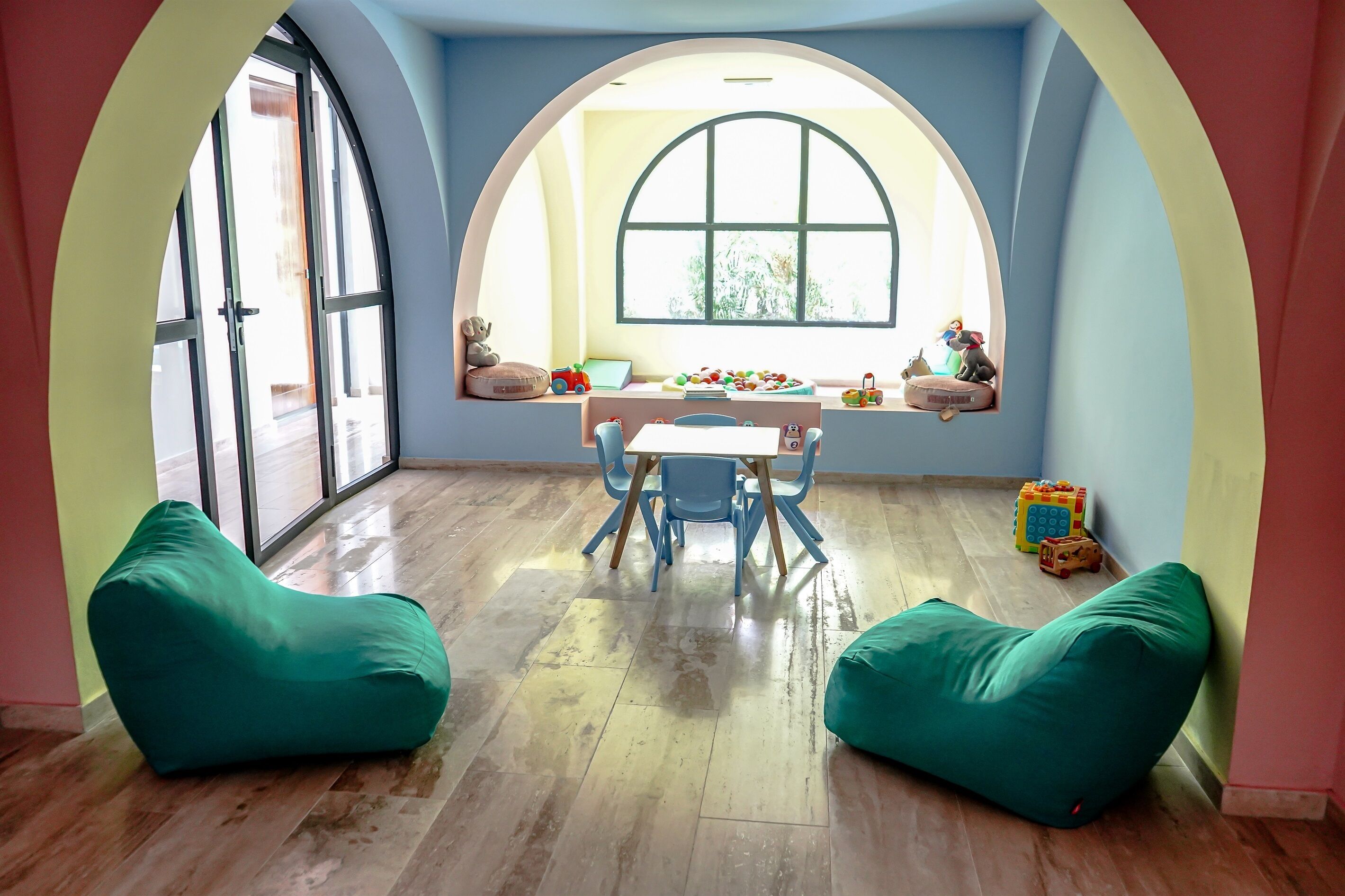 Ein Zimmer mit einem großen Bogenfenster, Holzboden, einem Tisch mit Stühlen und zwei Sitzsäcken.