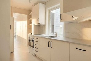 A modern kitchen with white cabinetry, a built-in oven, a window with blinds, and a stainless steel sink. - KS21 - 2BR Fairytale Bergen Hideaway (Bergen)