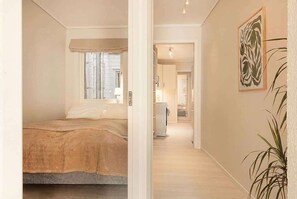 A bedroom with a bed, a window, a door leading to a hallway, and a plant. - KS21 - 2BR Fairytale Bergen Hideaway (Bergen)