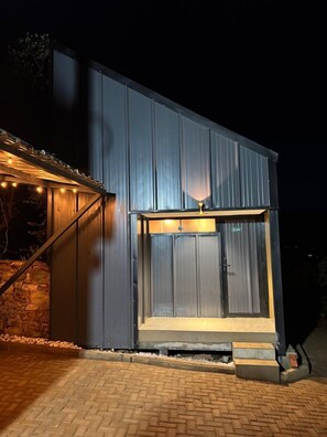 Un edificio moderno con un amplio ventanal, una terraza de madera y un muro de piedra.