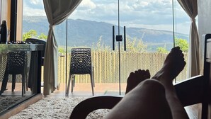 Een kamer met een groot raam, uitzicht op de bergen, een bed en een tafel met stoelen.
