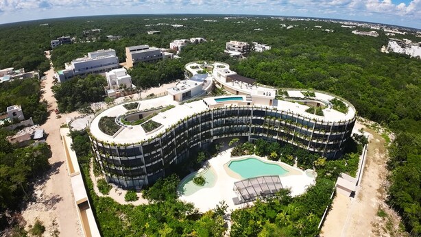Ein großes, rundes Hotel mit einem zentralen Pool, umgeben von üppiger Vegetation und weiteren Gebäuden.