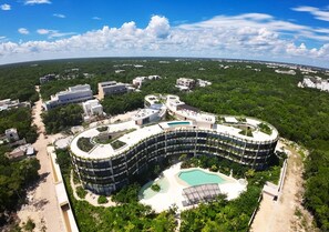 Un grand hôtel circulaire doté d’une piscine centrale, entouré d’une végétation luxuriante et d’autres bâtiments.