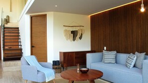 Ein modernes Wohnzimmer mit Sofa, Sessel, Couchtisch aus Holz und einer Treppe.
