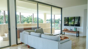 Un salon moderne avec un canapé gris, une table basse, un téléviseur à écran plat et un balcon doté de portes vitrées.