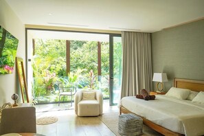 Ein Schlafzimmer mit Bett, Stuhl, Nachttisch und Blick auf Grün durch eine Schiebetür.