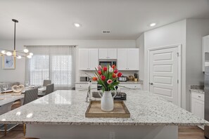 A modern kitchen with white cabinets, a granite island, and a vase of tulips.