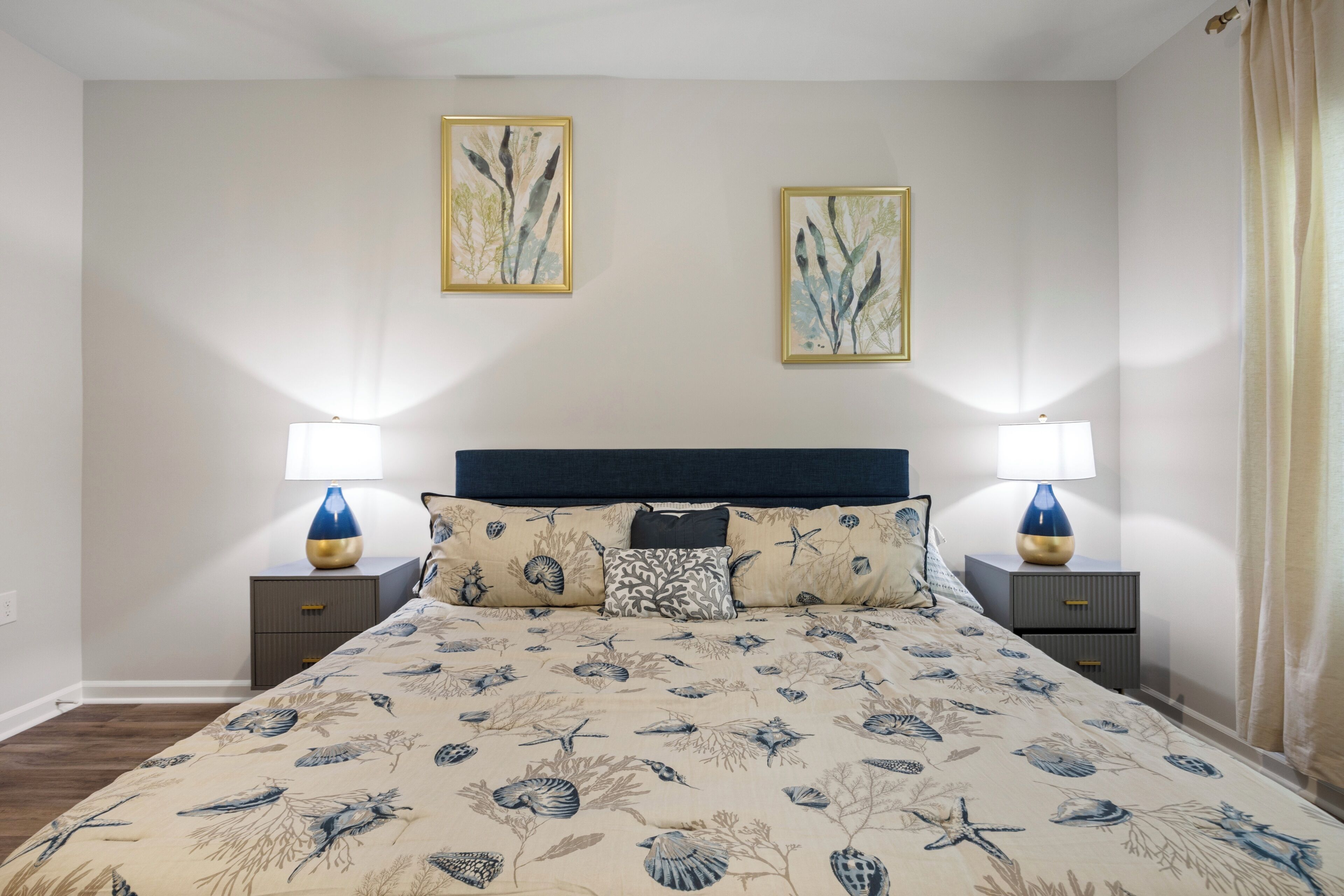 A bedroom with a bed, two nightstands, two lamps, and two wall-mounted paintings.