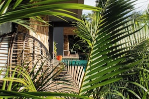 A pool area with a stone wall, wicker furniture, and lush greenery. - SwimUp Retreat in Aldea Zama Pool at Your Door & Beach Club (Tulum)