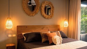 Ein Schlafzimmer mit einem Holzkopfende, zwei Wandspiegeln, einem Bett mit vielen Kissen und zwei Wandleuchten.