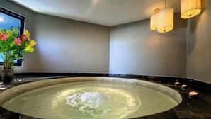 Ein Wellnessraum mit Whirlpool, Wandleuchten und einer Topfpflanze.