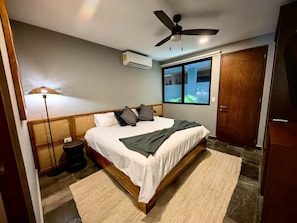 Une chambre à coucher comprenant un lit, un ventilateur de plafond, un appareil de climatisation, une fenêtre et une porte.
