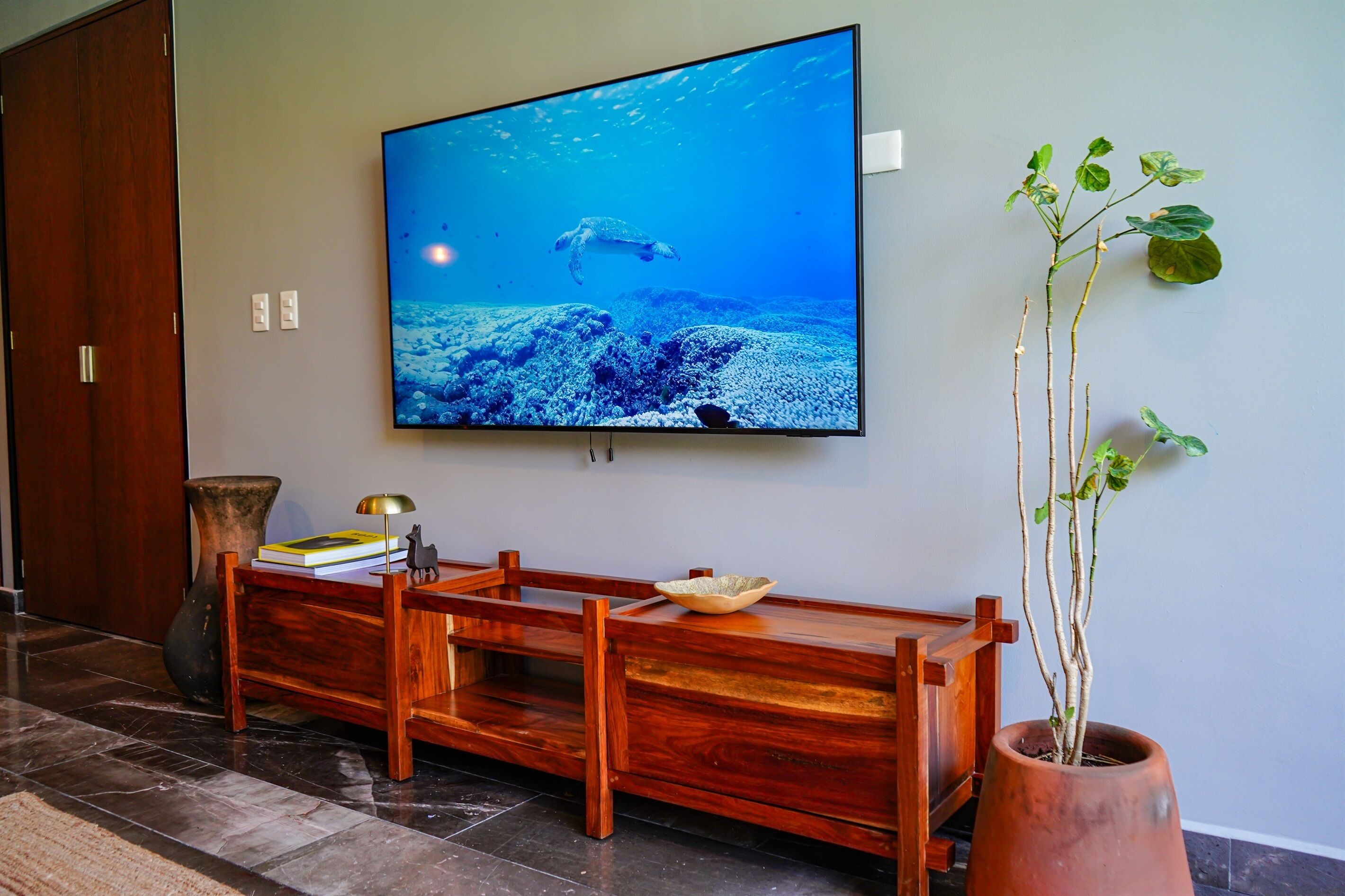 A room with a television displaying an underwater scene, a wooden bench, a potted plant, and a vase.