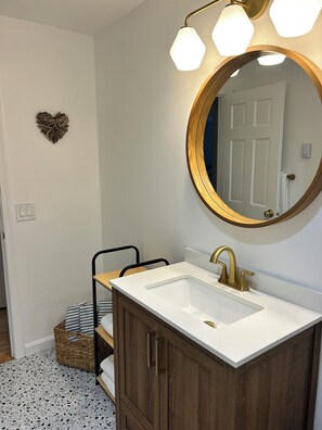 Une salle de bain avec un lavabo blanc, un robinet doré et un miroir rond doté de trois lampes.
