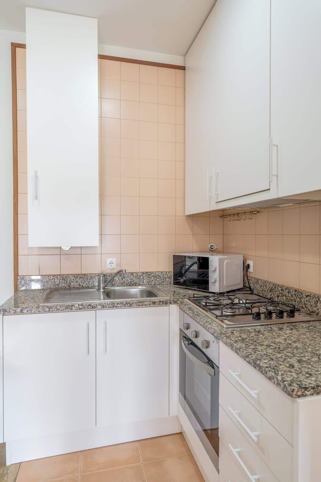 Une cuisine avec des meubles blancs, un plan de travail en granit, une cuisinière, un four à micro-ondes et un évier.