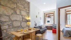 Ein gemütliches Wohnzimmer mit Steinwand, einer Essecke mit Tisch und Stühlen sowie einer Couch.