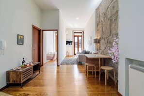 Ein Flur, der in einen Essbereich mit Steinwand, einem Holztisch und einer Couch führt.