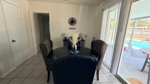 Een eetruimte met een ronde tafel, stoelen, een klok en uitzicht op een zwembad.