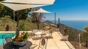 Ein Poolbereich mit Liegestühlen, einem Tisch mit Obstkorb und Blick auf das Meer.