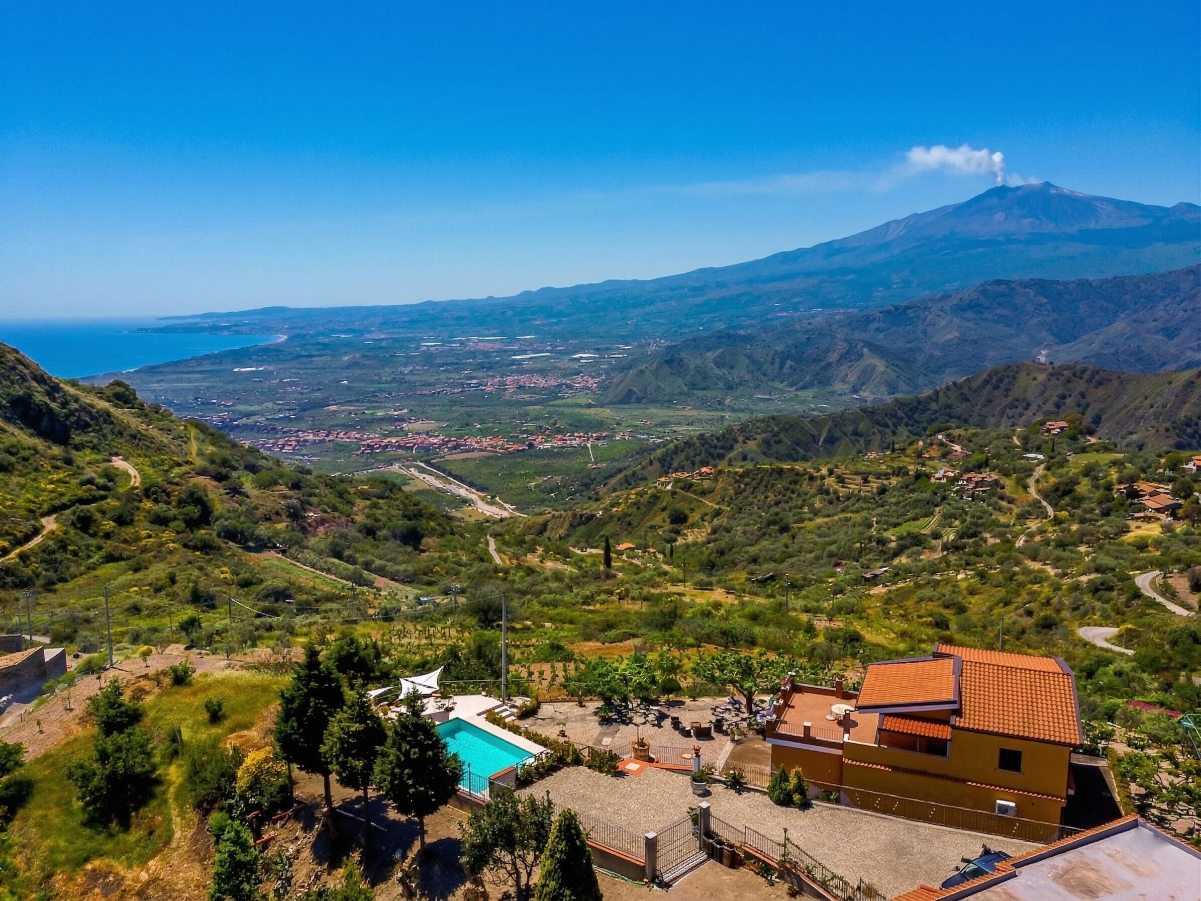 Une villa avec piscine, entourée d’une végétation luxuriante et offrant une vue sur une montagne lointaine.