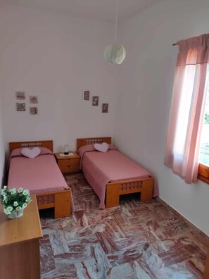 Ein Zimmer mit zwei Betten, einem Nachttisch, einer Pendelleuchte und einem Fenster mit Vorhängen.