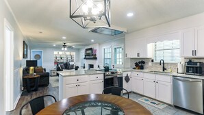 A modern kitchen with white cabinets, a central island, stainless steel appliances, and a dining area with a glass table. - Hot Tub, Pool Table, Ping-Pong, Private Playground, Fire Pit, Library, Play Room (Valdosta)