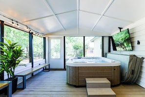 Un espace extérieur abrité comprenant un jacuzzi, des bancs en bois et une plante en pot.