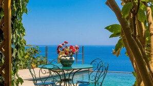 Une table entourée de chaises et ornée d’un vase de fleurs, avec une vue imprenable sur une mer bleue et limpide.
