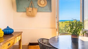 A room with a wooden table, a chair, a hanging shelf with a hat and bag, and a view of the sea. - Villa Tiaréa - Giarre (Giarre)
