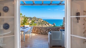 Un umbral abierto que da a un patio con una mesa preparada para dos, una silla de mimbre y un muro de piedra.