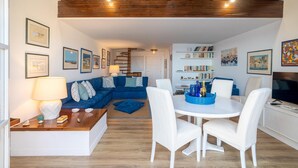 Una sala de estar moderna con un sofá azul, sillas blancas, una mesa de comedor y un televisor.