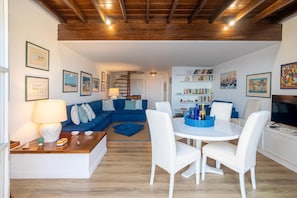 Una sala de estar moderna con un sofá azul, sillas blancas, una mesa de comedor y un televisor.