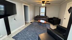 A living room with a ceiling fan, a flat-screen TV mounted on the wall, a sofa, a coffee table, and a rug. - H1-Large 3 Bedroon 1.5 Bathroom apartment (Syracuse)