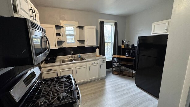 A compact kitchen with a stove, microwave, and refrigerator, featuring light wood flooring and white cabinetry. - H1-Large 3 Bedroon 1.5 Bathroom apartment (Syracuse)